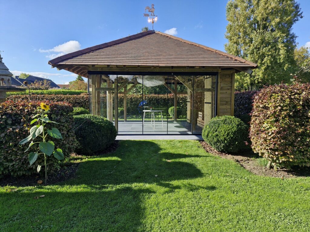 Tuinhuis met glazen schuifwanden die het interieur verbinden met de tuin, voor een lichte en beschutte buitenruimte het hele jaar door.