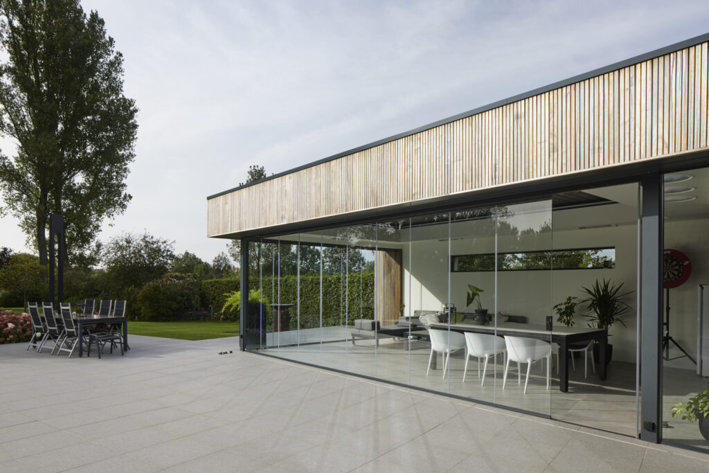Glazen schuifwand ONE die een moderne leefruimte verbindt met het terras en zorgt voor een open uitzicht op de tuin
